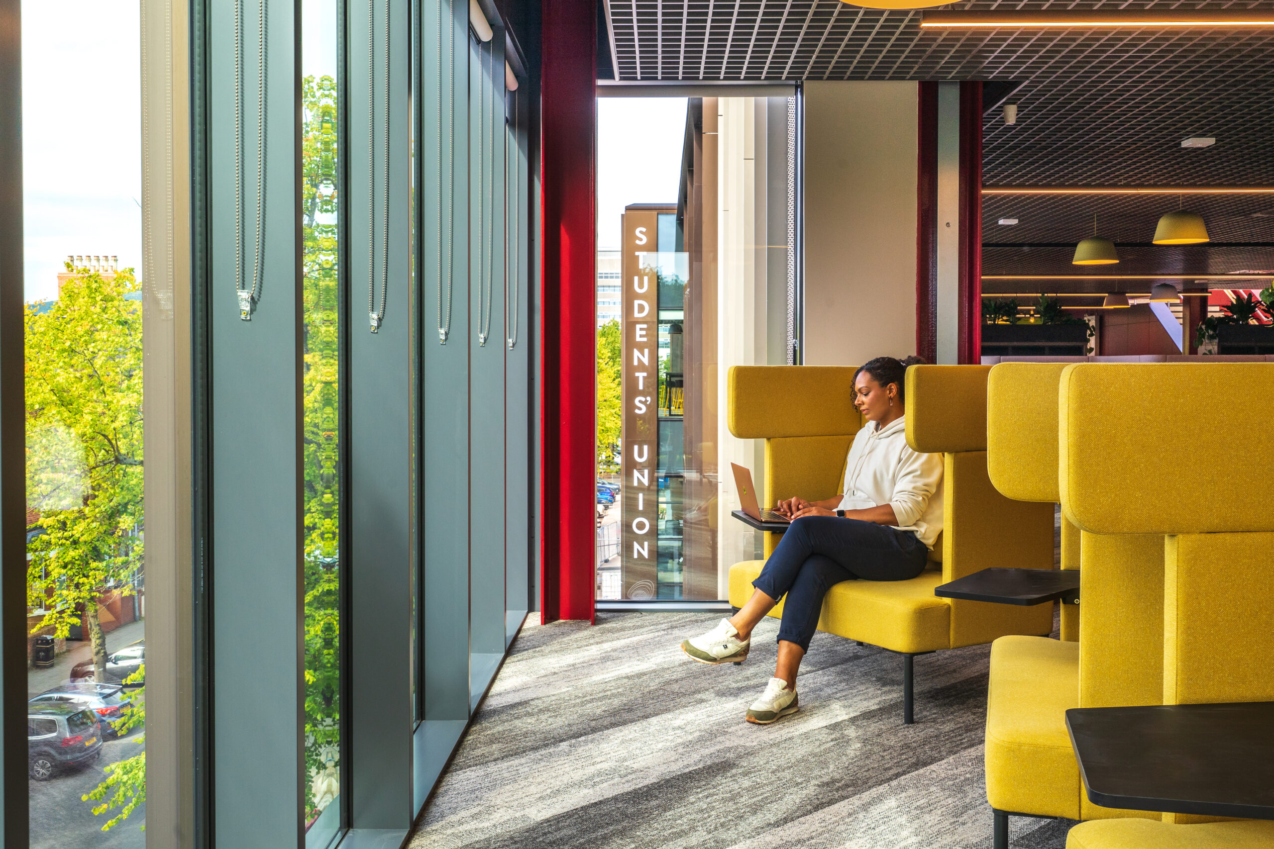 A woman is sitting on one of several yellow Ocee and Four Design office work booths.